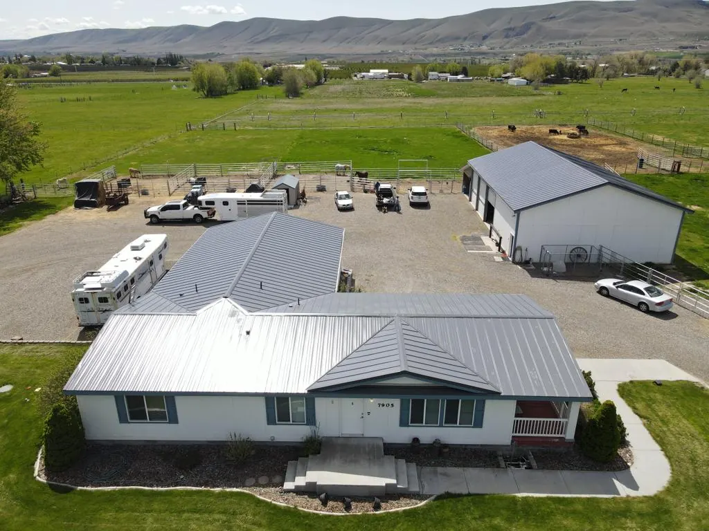 Aerial view of a gray metal roof on a single-story home, with a large shop building and open farmland behind it