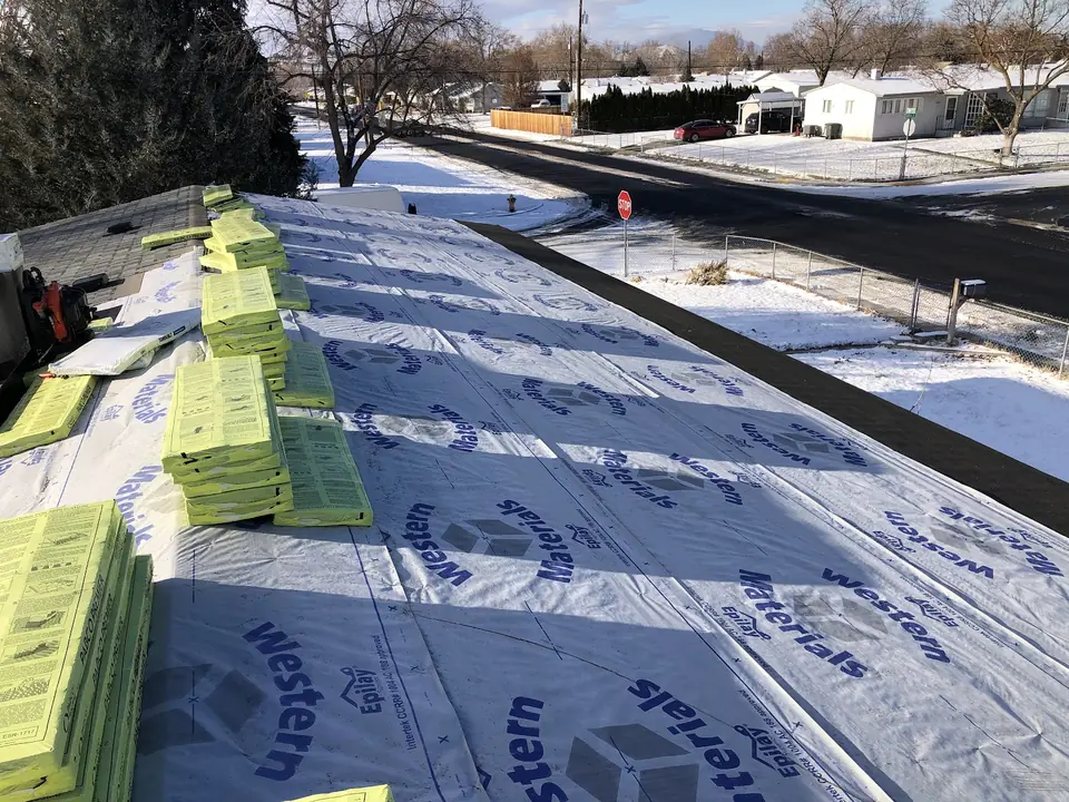 Synthetic underlayment rolled out across a roof during a winter re-roof, with snow on the ground below