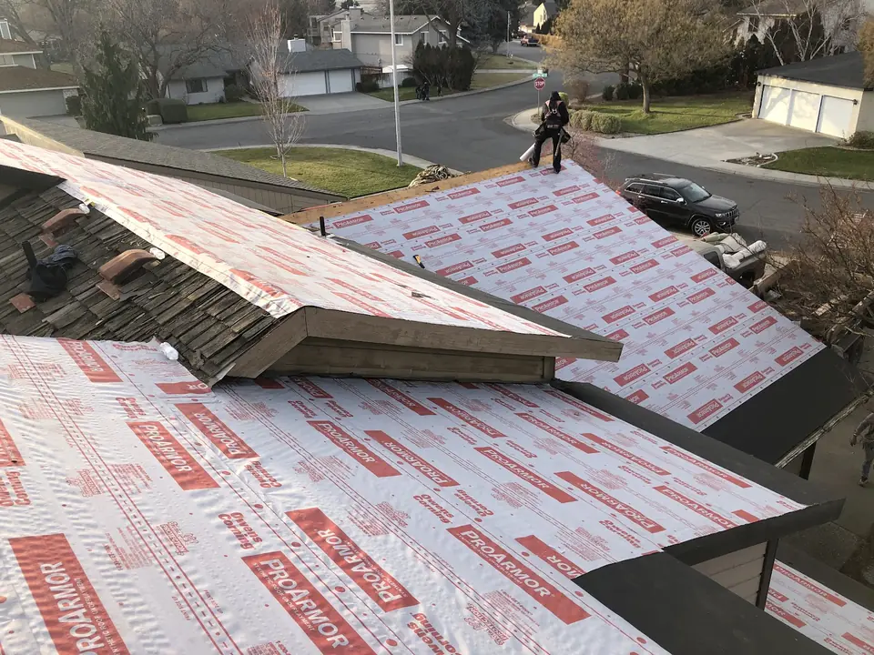 Old wood shakes being torn off a roof while new underlayment goes down over the decking